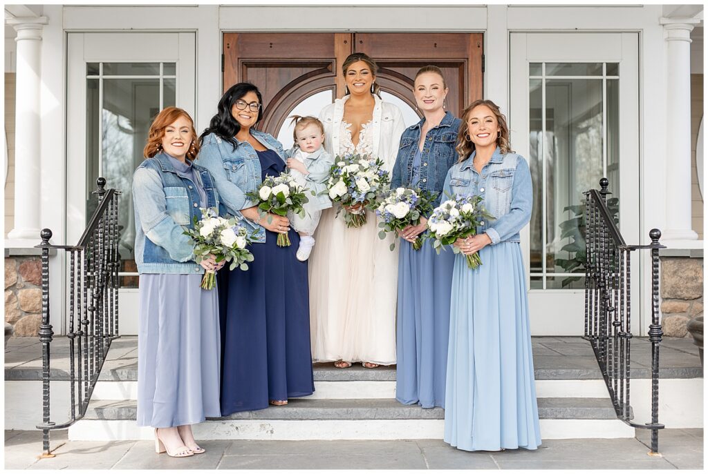 bride with her four bridesmaids all wearing shades of blue gowns and blue jean jackets on steps of rivercrest golf club
