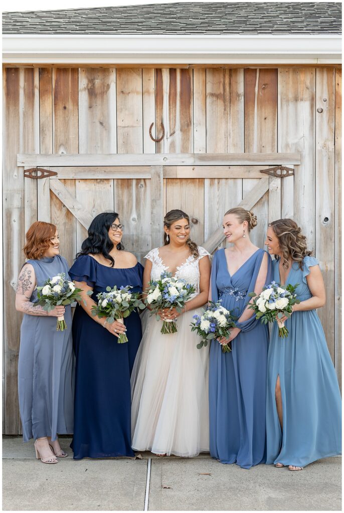bride with her four bridesmaids as they all smile and look at each other by large wooden door at rivercrest golf club