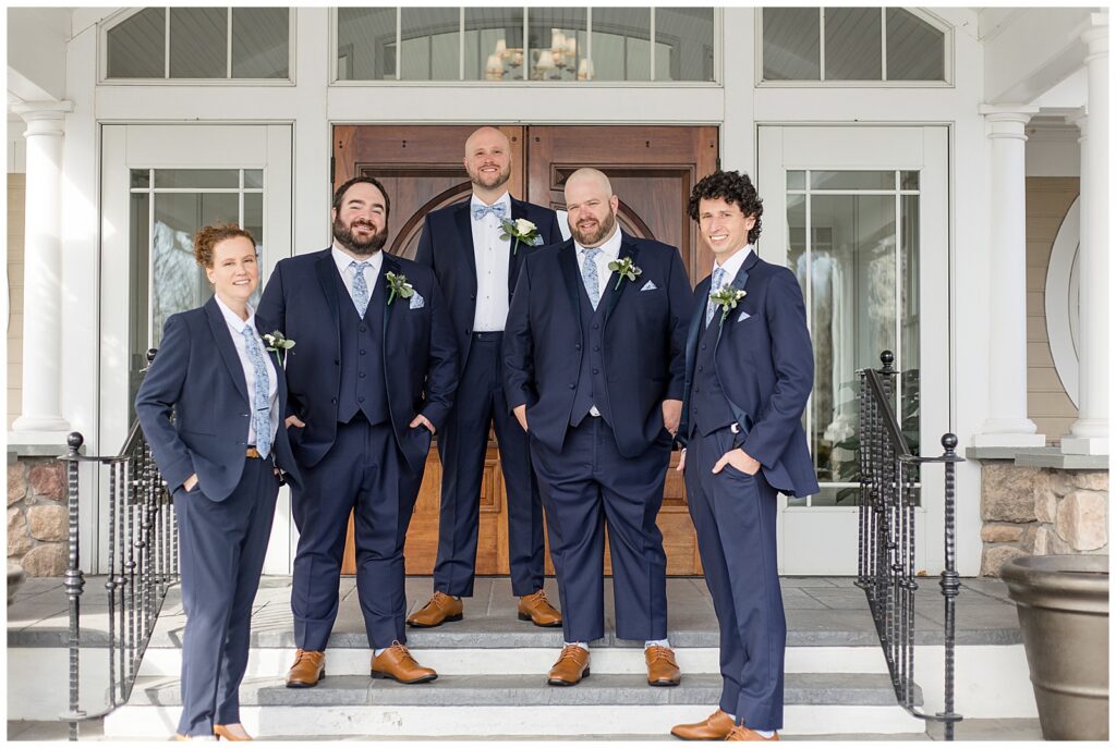 groom standing with his four groomsmen all wearing blue suits on steps of rivercrest golf club