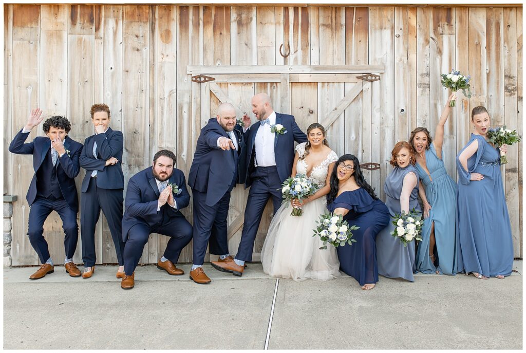 bride and groom with their bridal party as everyone is striking funny poses by large wooden door at golf club in montgomery county pennsylvania