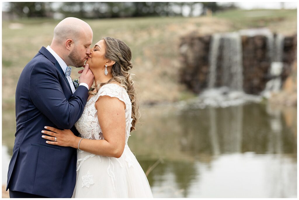 groom kissing his bride at rivercrest golf club with waterfall and pond behind them