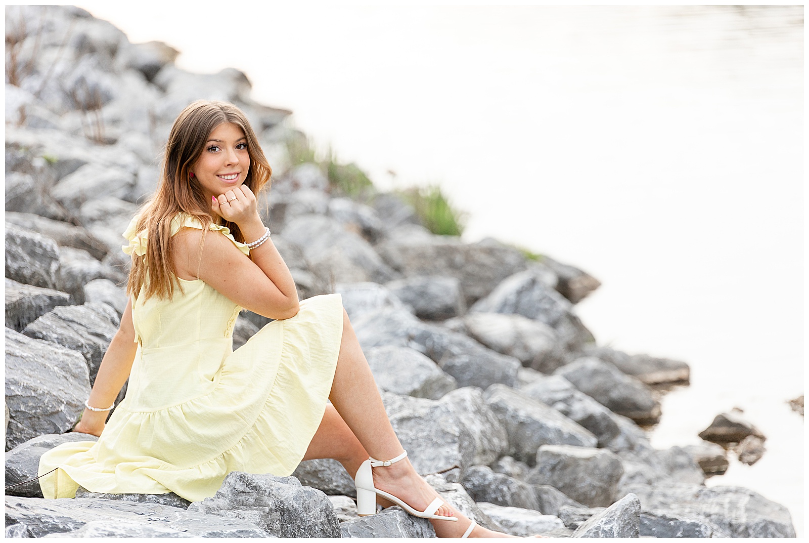senior girl in yellow dress sitting on gray rocks with her right elbow on her right knee at speedwell forge lake