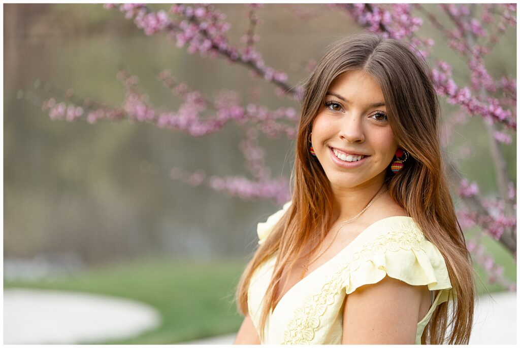 senior spokesmodel smiling at camera by purple budding tree at speedwell forge lake in lancaster county