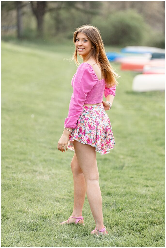 senior girl in vibrant pink top with floral skirt by colorful canoes at speedwell forge lake
