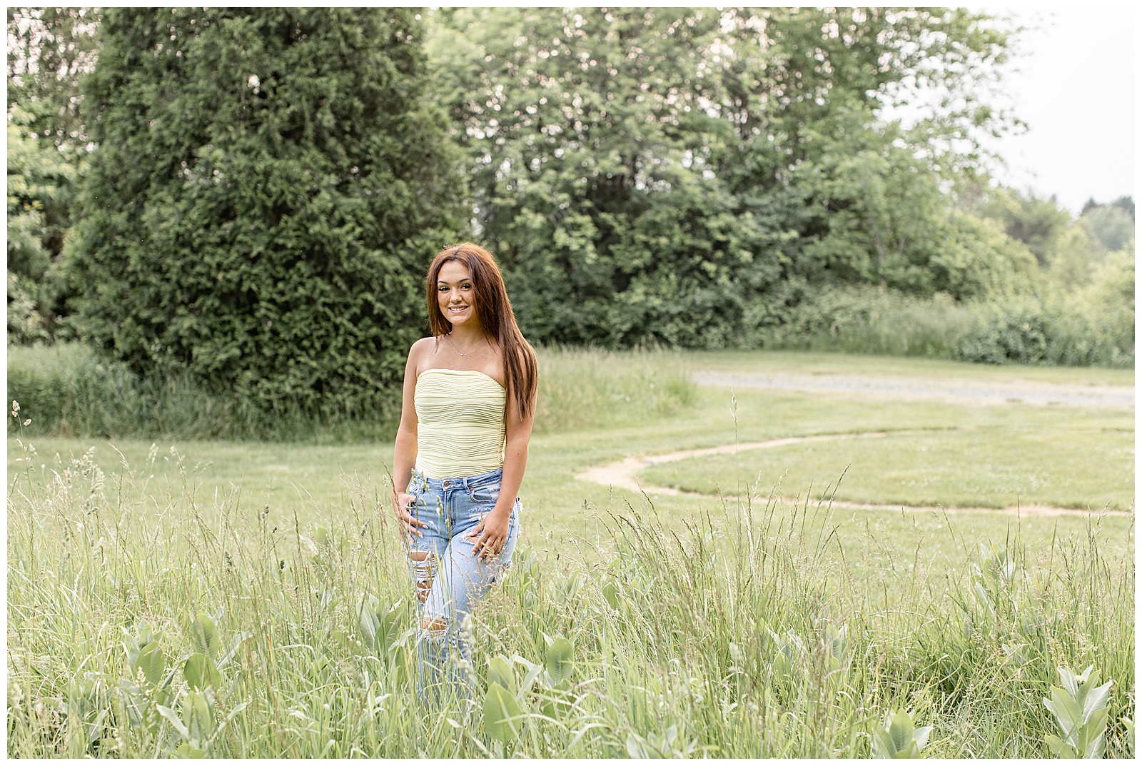 senior girl in light yellow tank top and blue jeans standing in tall wild grasses at overlook park in lancaster pa