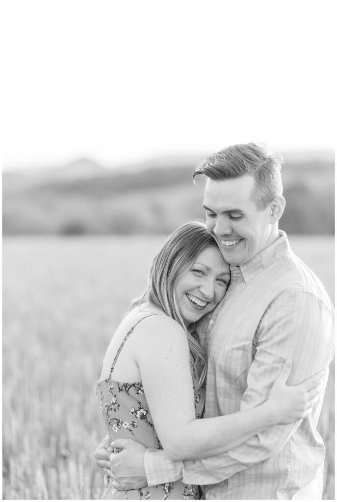 black and white photo of couple standing in wheat field as woman lays her left cheek on guy's chest in central pennsylvania
