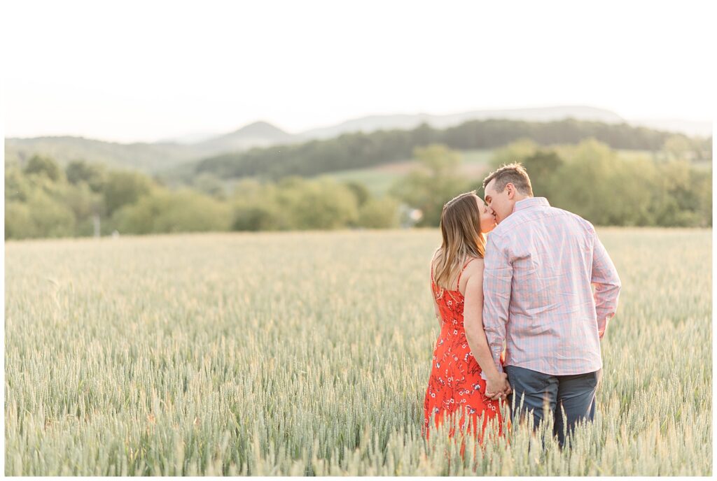 engaged couple holding hands with their backs toward the camera as they kiss in wheat field in pennsylvania