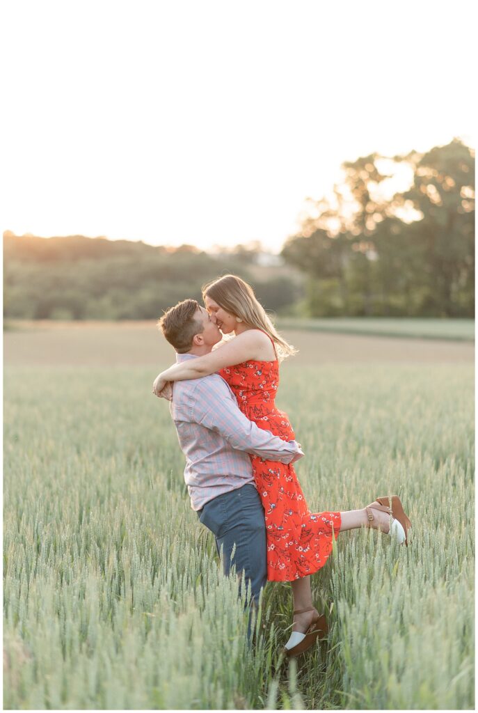 guy lifting up his fiance as they kiss in wheat field at sunset in central pennsylvania