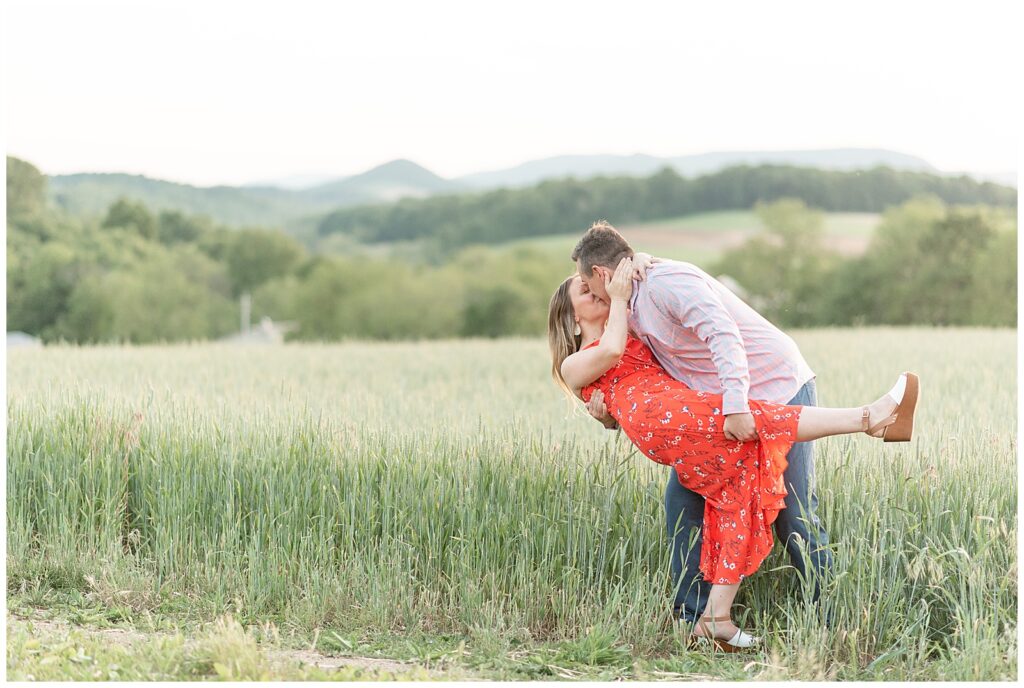 man dipping backing his fiance as they kiss at edge of wheat field with mountains in the background in pennsylvania
