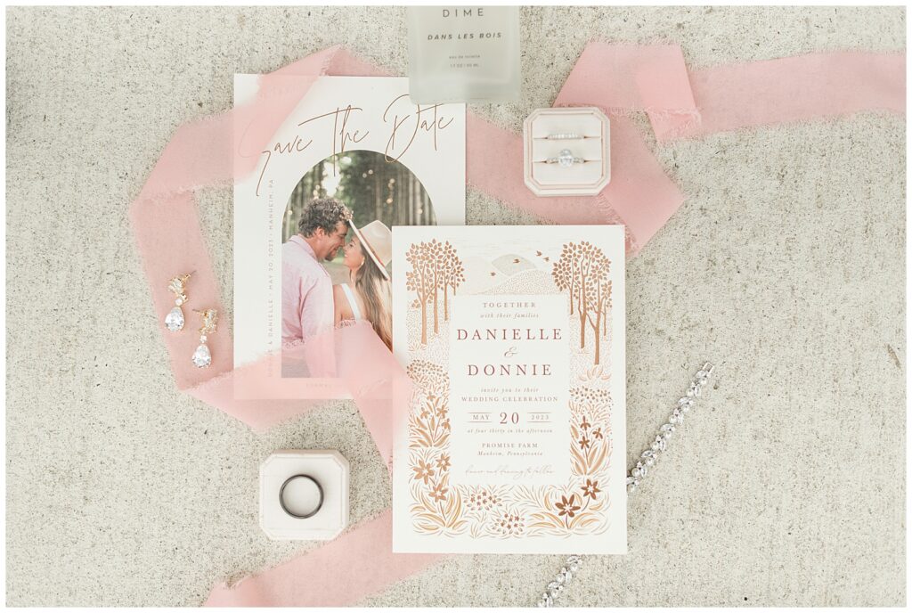 wedding invitation and boxes of wedding rings displayed with light pink ribbon at promise farm