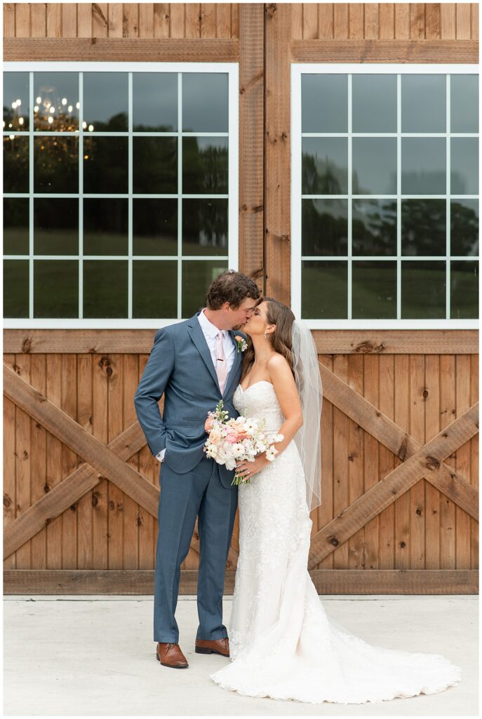 bride and groom kiss in front of large barn doors at beautiful promise farm in lancaster county pennsylvania