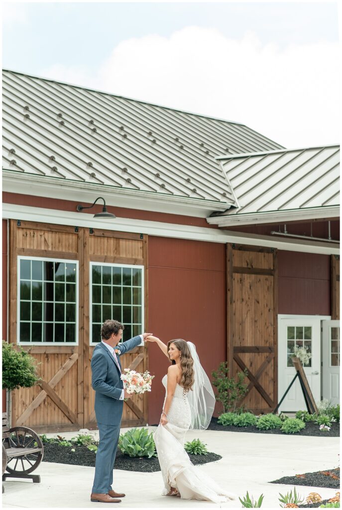 groom twirls his bride by large barn doors on sunny spring day at manheim wedding venue