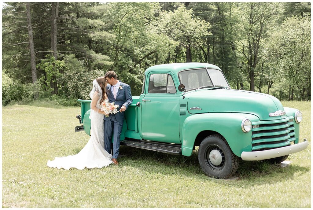 couple stands close with foreheads touching as groom leans against vintage green pickup truck at promise farm