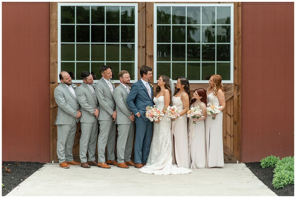 couple with their bridal party all looking towards bride and groom who are looking at each other by barn doors in lancaster county