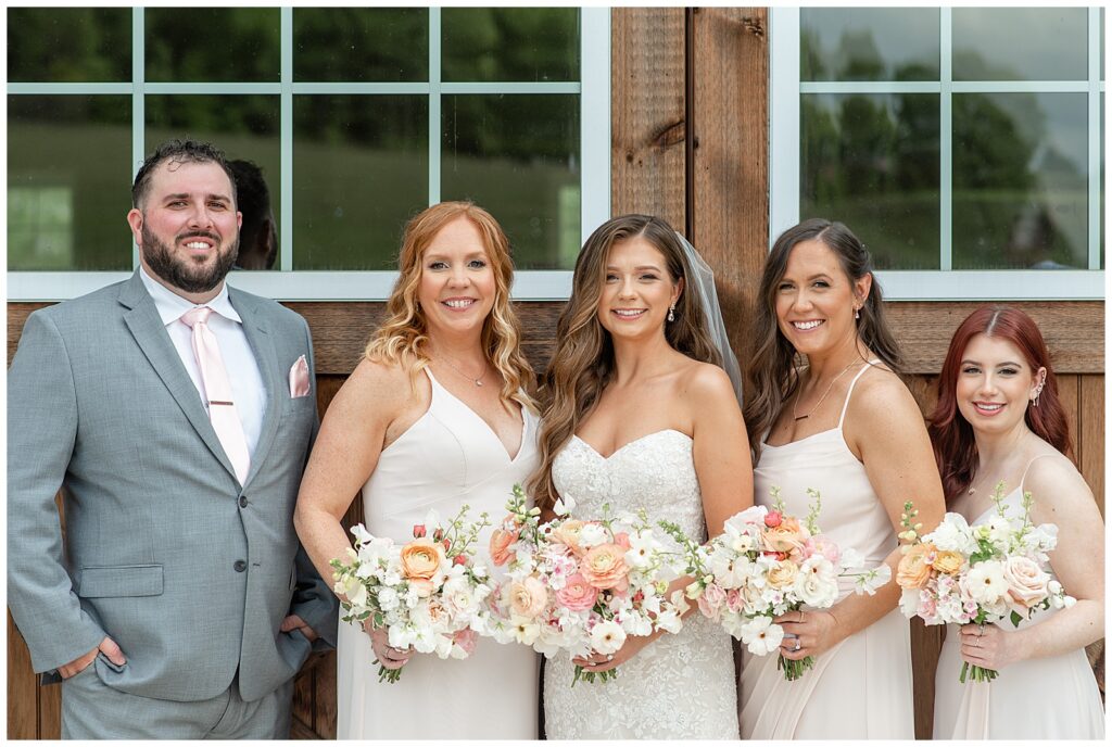 bride with her two bridesmaids and one groomsman in front of barn door at promise farm