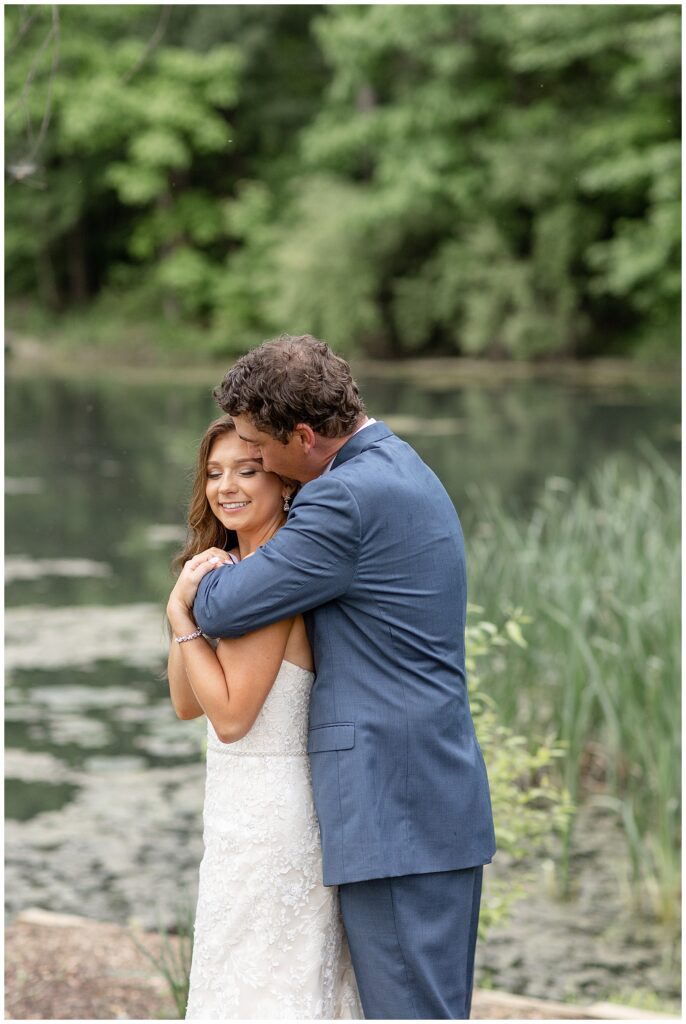 groom hugging and kissing his bride from behind by pond at promise farm in lancaster county