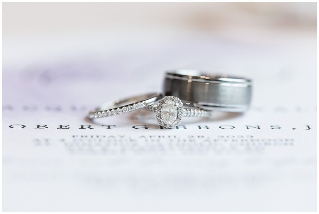 silver bride's wedding ring and groom's wedding band resting on top diamond engagement ring in maryland