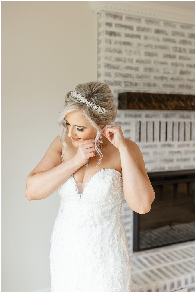 bride adjusting her left earring in strapless white wedding gown by fireplace in maryland
