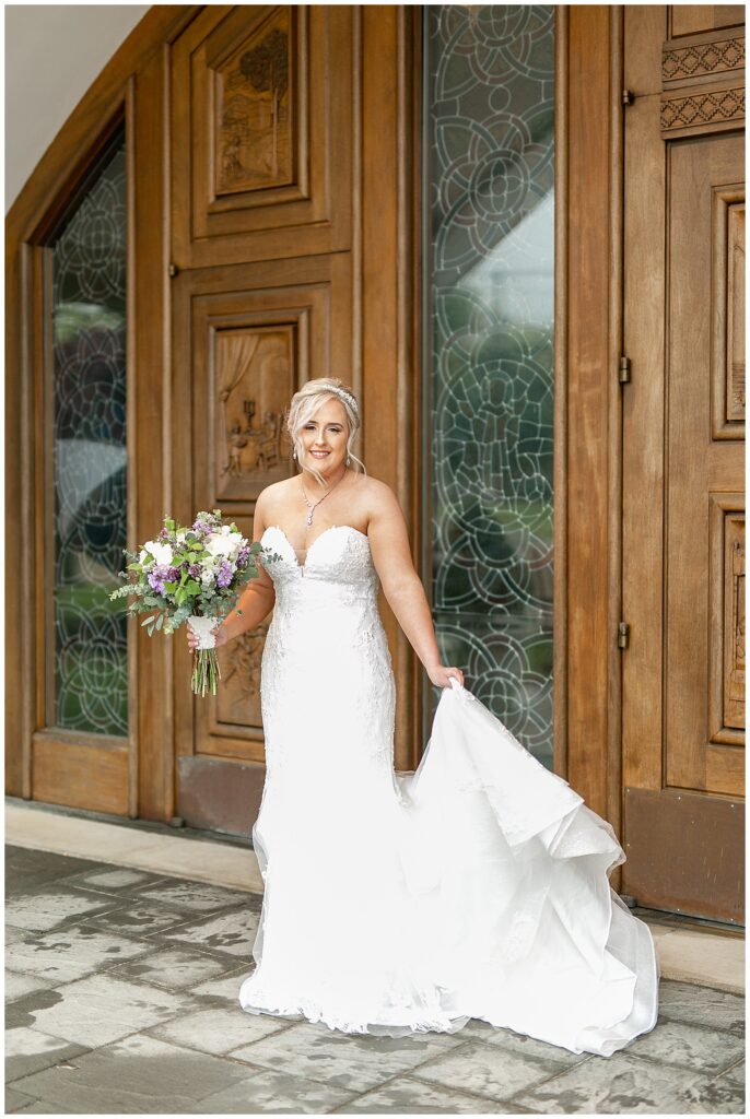 bride holding her bouquet in right hand and dress train in left hand by large wooden doors at Saint Ignatius Catholic Church