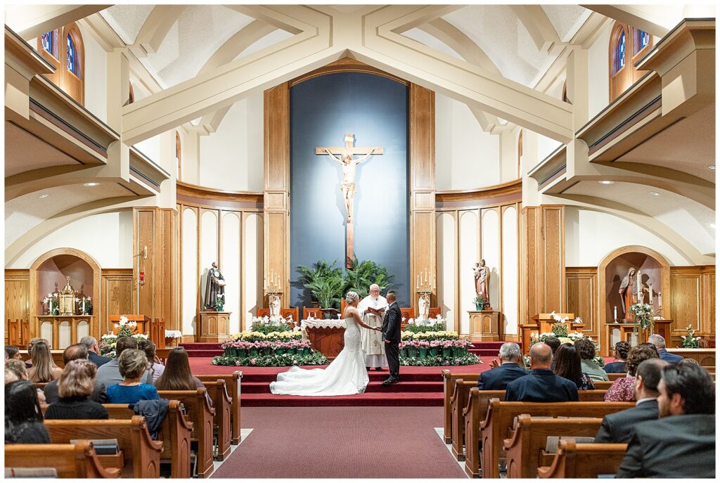 bride and groom hold hands by their priest during wedding ceremony in the lovely Saint Ignatius Catholic Church