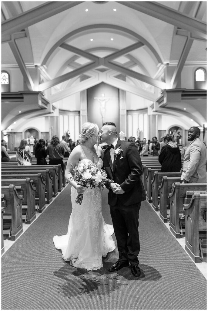 black and white photo of couple kissing at the back of the church as guests watch from pews at Saint Ignatius Catholic Church