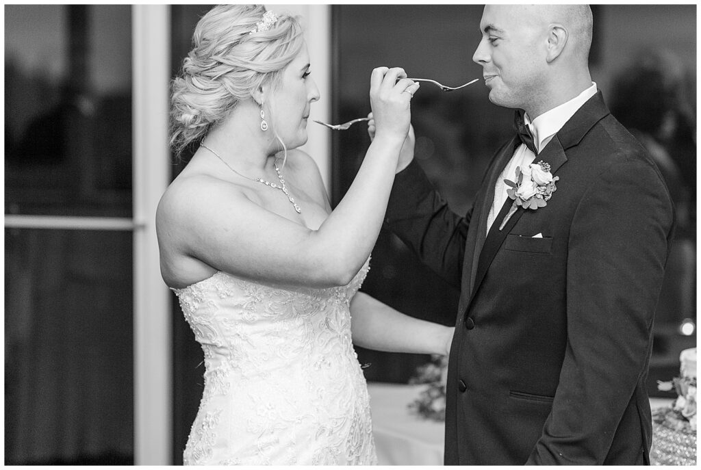 black and white photo of bride and groom feeding one another their wedding cake with forks at maryland golf and country club