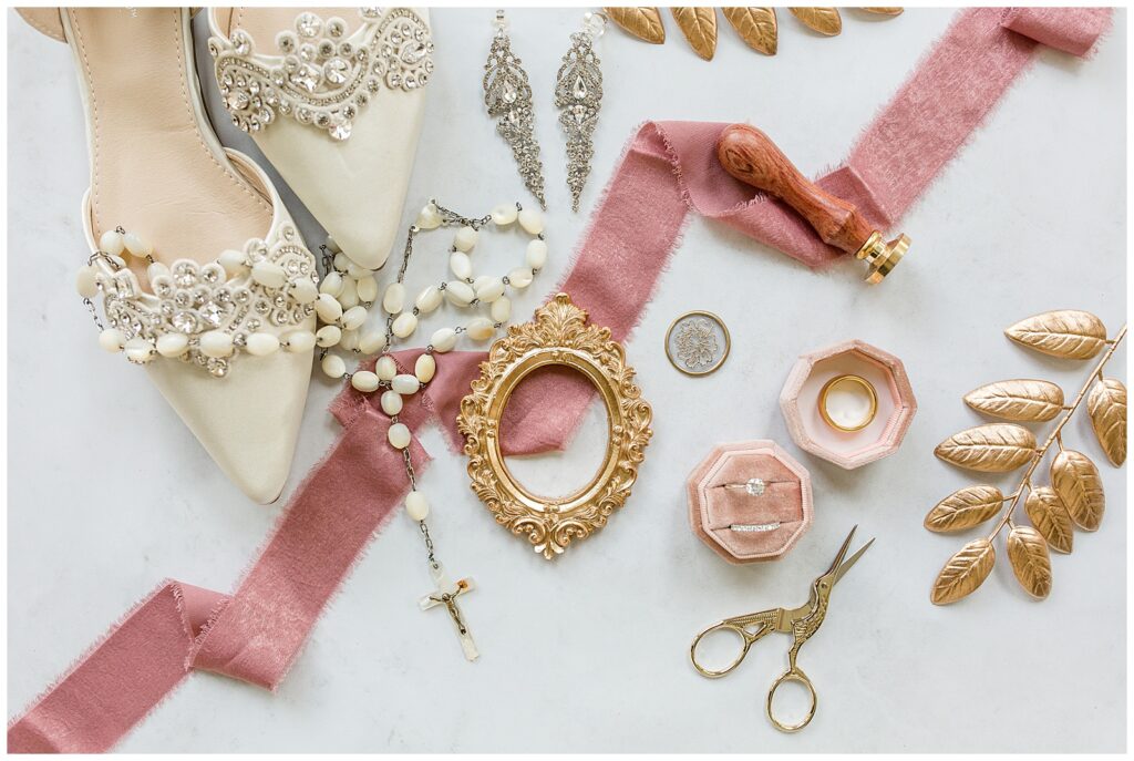 wedding rings in pink velvet box surrounded by a rosary, earrings, bride's shoes, and gold and pink accents at the shrine of anthony