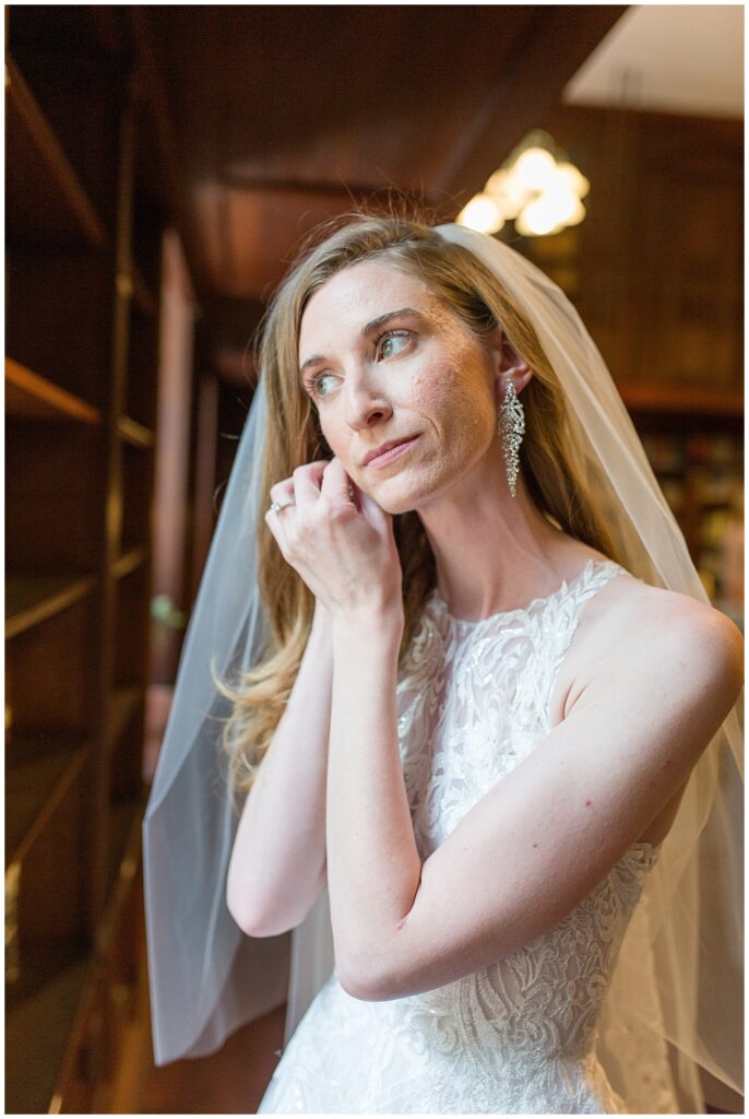 bride adjusting her right earring as she looks to her right wearing halter top bridal gown and veil at the shrine of anthony