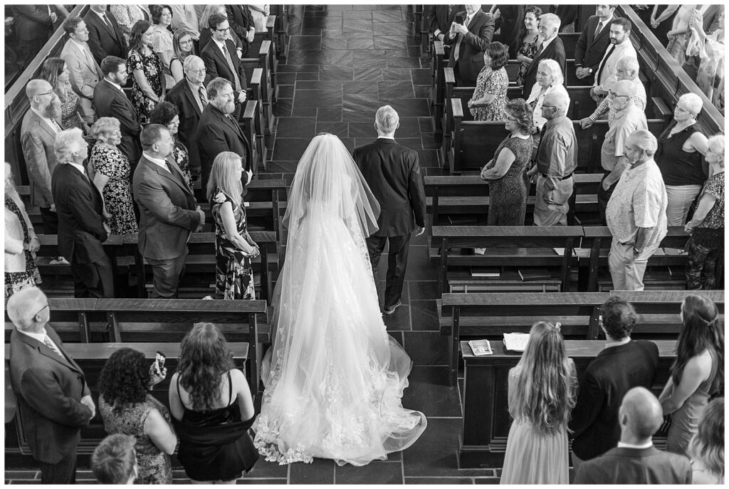black and white photo from above of the backs of the bride and her father and he walks her down the aisle inside the shrine of saint anthony