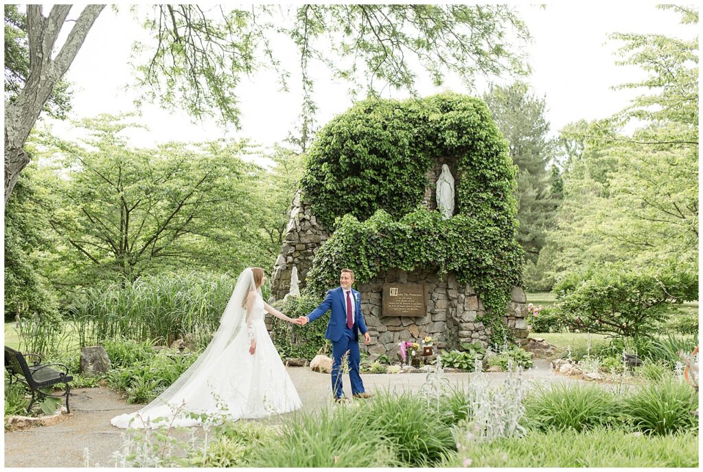 groom leading his bride along pathway of beautifully landscaped garden with ivy at the shrine of saint anthony