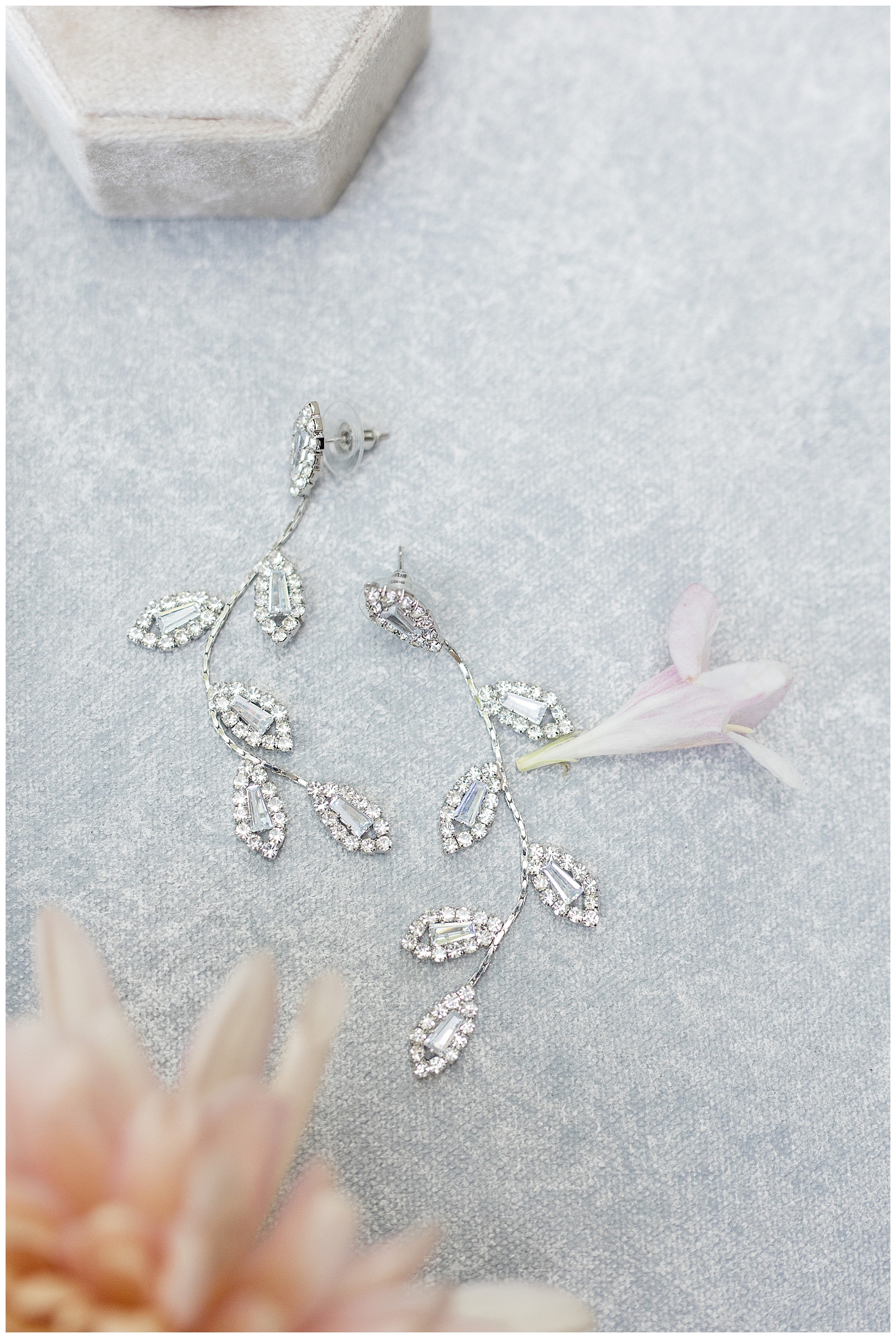 bride's unique long diamond earrings displayed on gray background with flower petals at the barn at silverstone