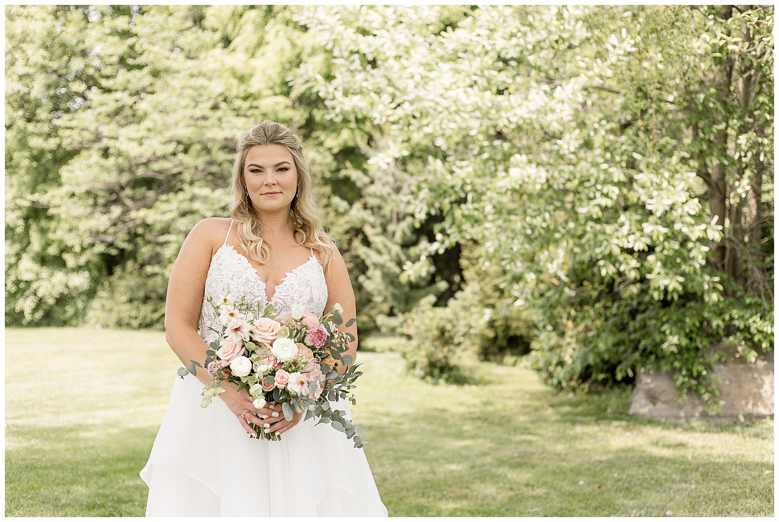bride standing to the left of photo and barely smiling as she holds her bouquet outdoors at the barn at silverstone