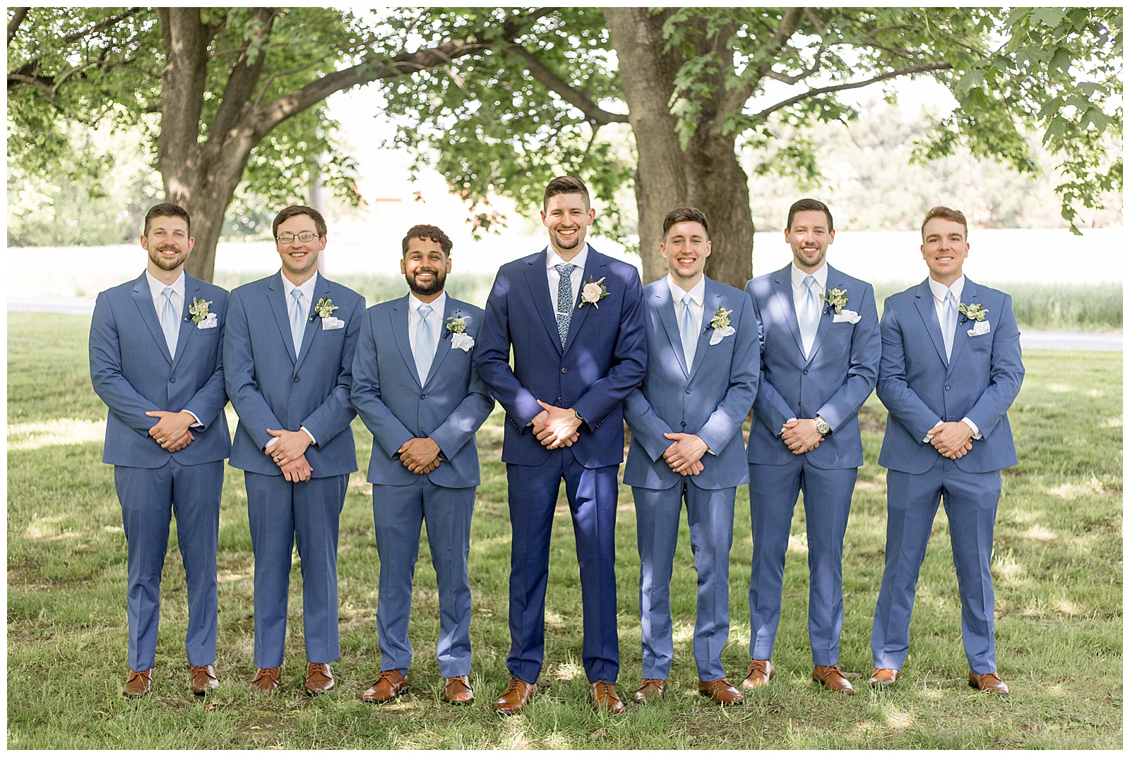 groom standing with his six groomsmen all in navy blue suits standing in a row outdoors at the barn at silverstone