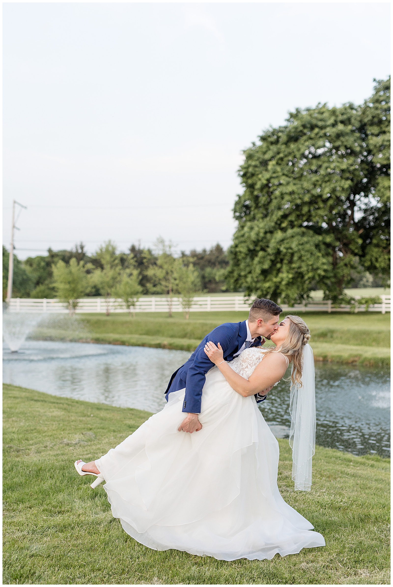 groom dips his bride back by beautiful pond at the barn at silverstone on spring day