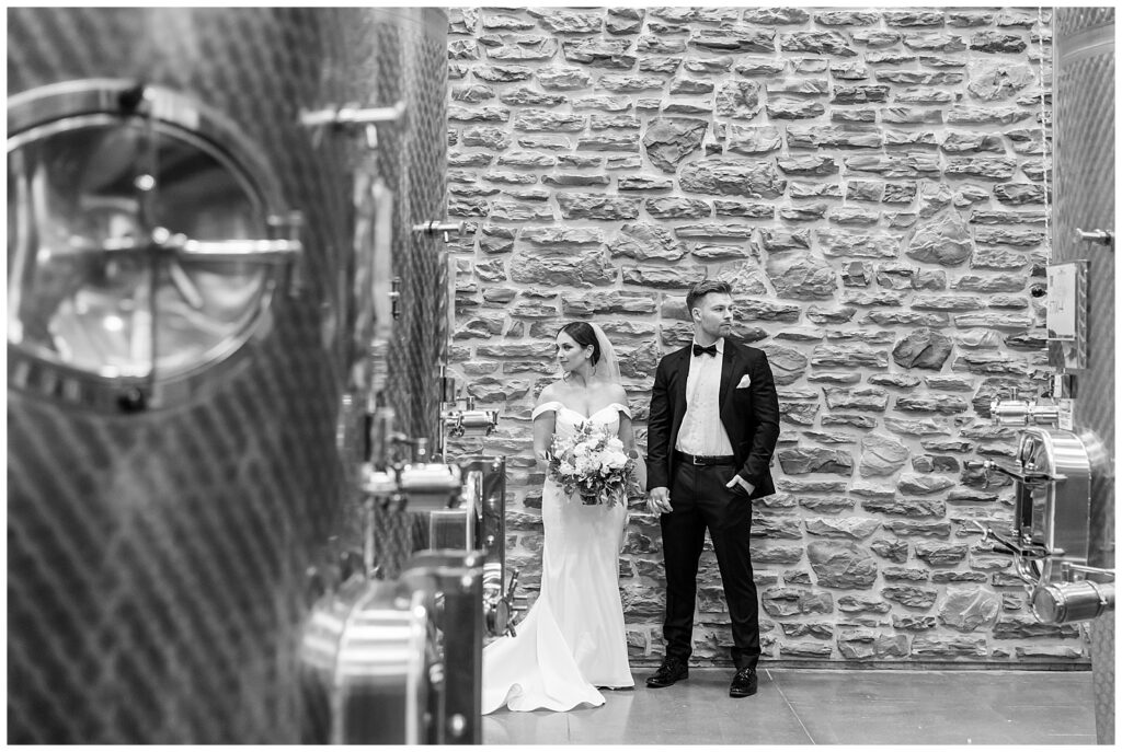 black and white photo of couple looking in opposite directions as they stand in front of stone wall at folino estate winery