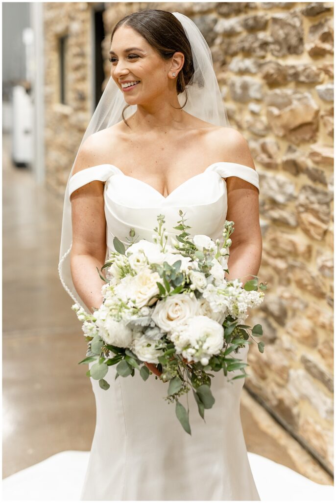 close up photo of bride wearing off the shoulder gown and holding stunning bouquet of white flowers and eucalyptus at winery in berks county pennsylvania