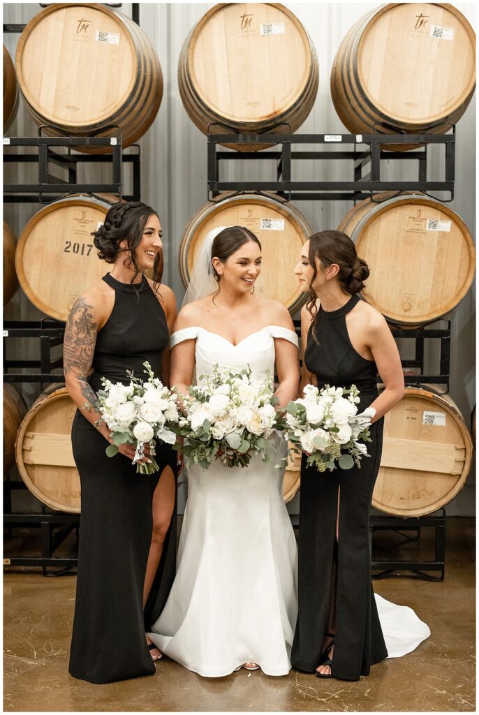 bride with her two bridesmaids standing by wooden barrels indoors at folino estate