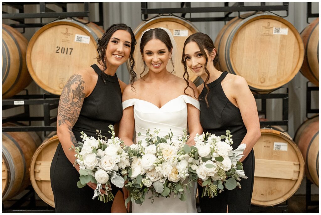 bride in white gown with her two bridesmaids who are wearing black dresses holding their bouquets at winery 