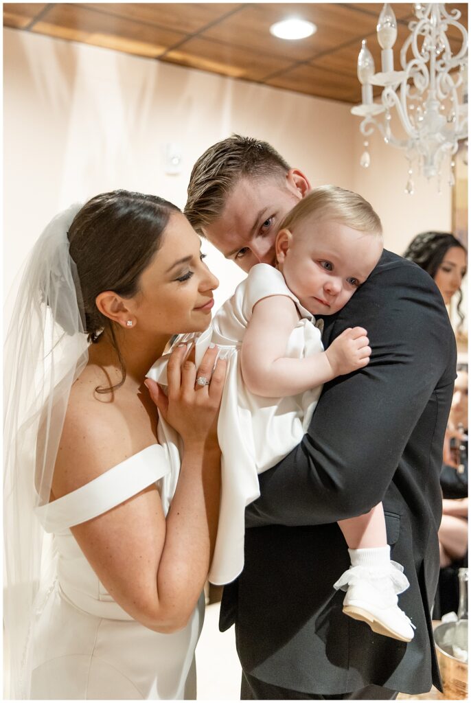 groom holding the couple's baby girl as bride snuggles close during special moment on their wedding day at folino estate