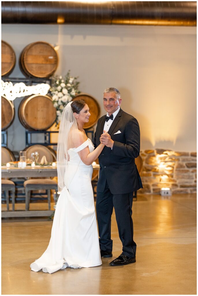 bride and her father dancing during reception with wooden barrels behind them at folino estate in pennsylvania