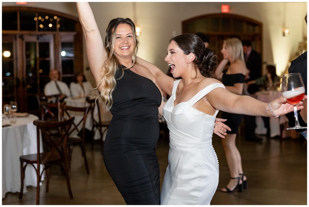 bride and her friend celebrate with raised arms as they dance during reception at folino estate in berks county