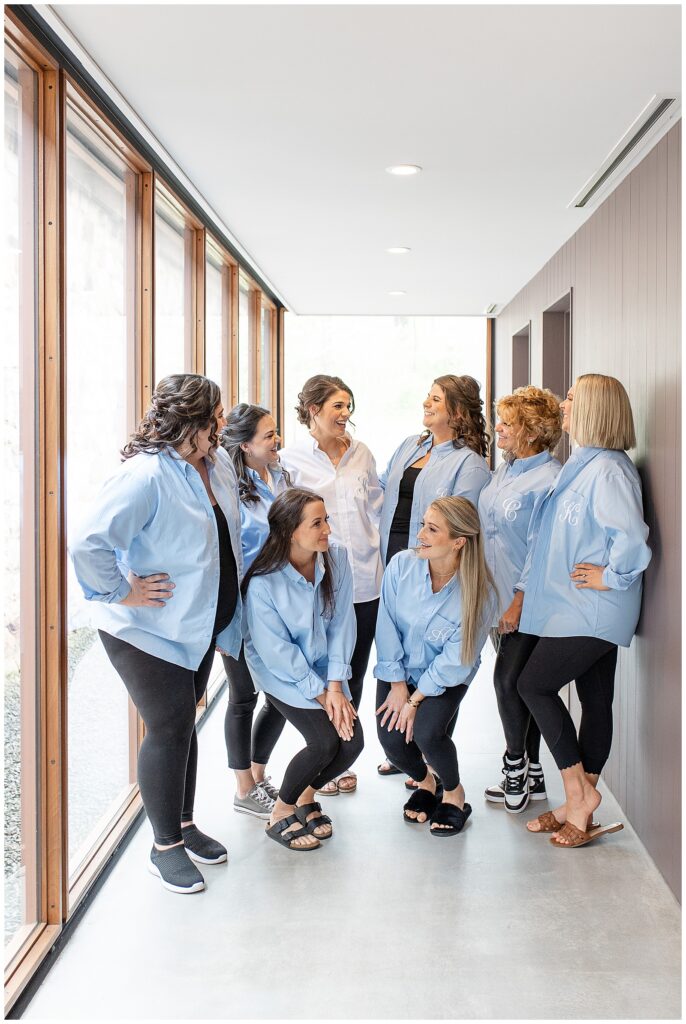 bride surrounded by her seven bridesmaids all in matching blue shirts and black pants in bridal suite at elizabeth furnace