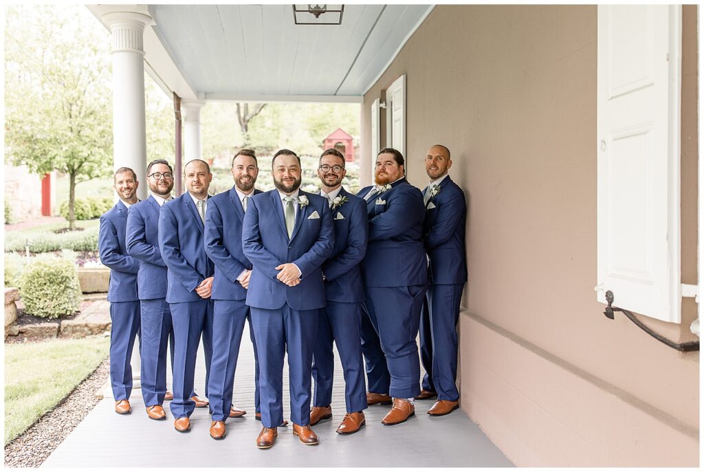 groom with his seven groomsmen all wearing dark blue suits standing in a V on front porch at elizabeth furnace
