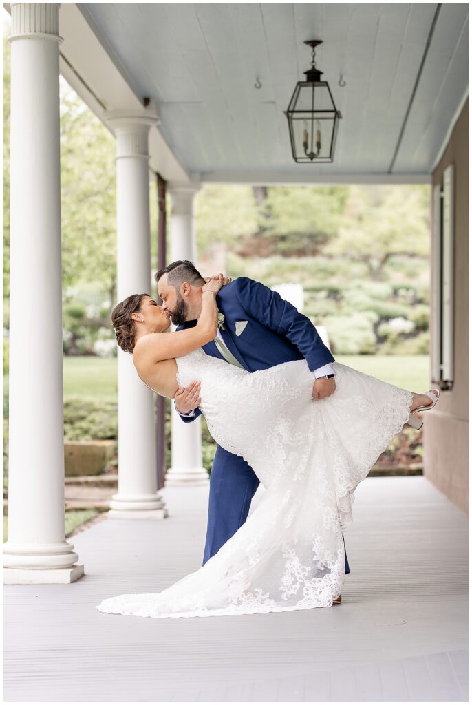 groom dips his bride back as they kiss on front porch at elizabeth furnace