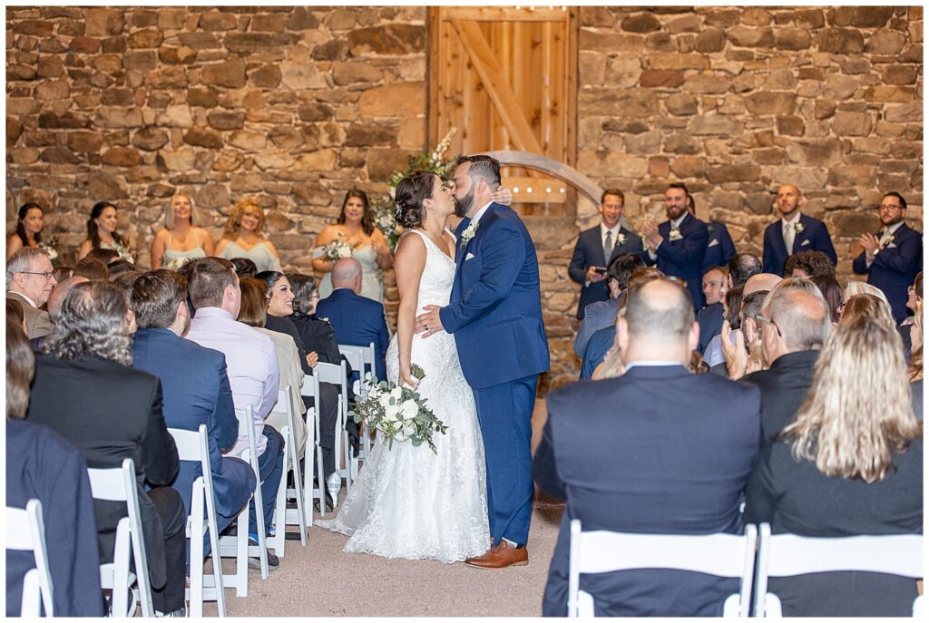 bride and groom share their first kiss during indoor wedding ceremony at elizabeth furnace in lititz pa