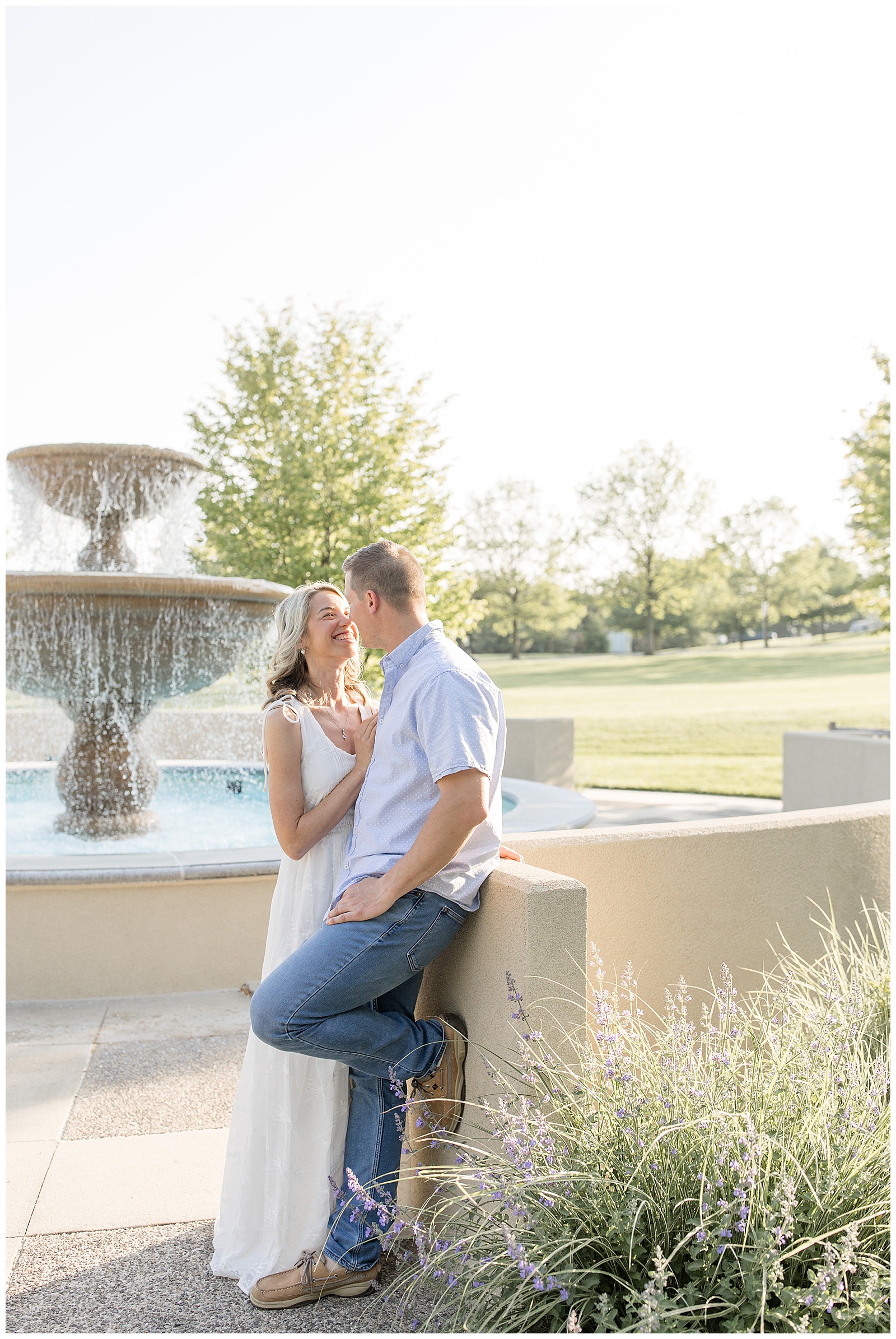 man leaning against concrete wall as he's almost kissing his bride-to-be by fountain at masonic village