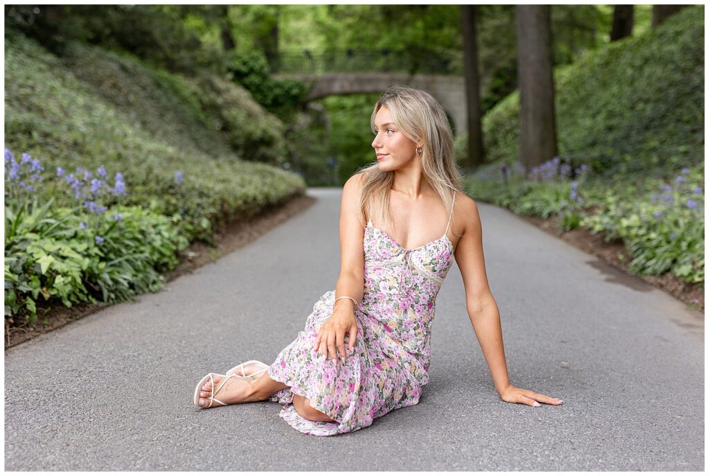 senior girl sitting on paved pathway in shaded area of longwood gardens and looking over her right shoulder