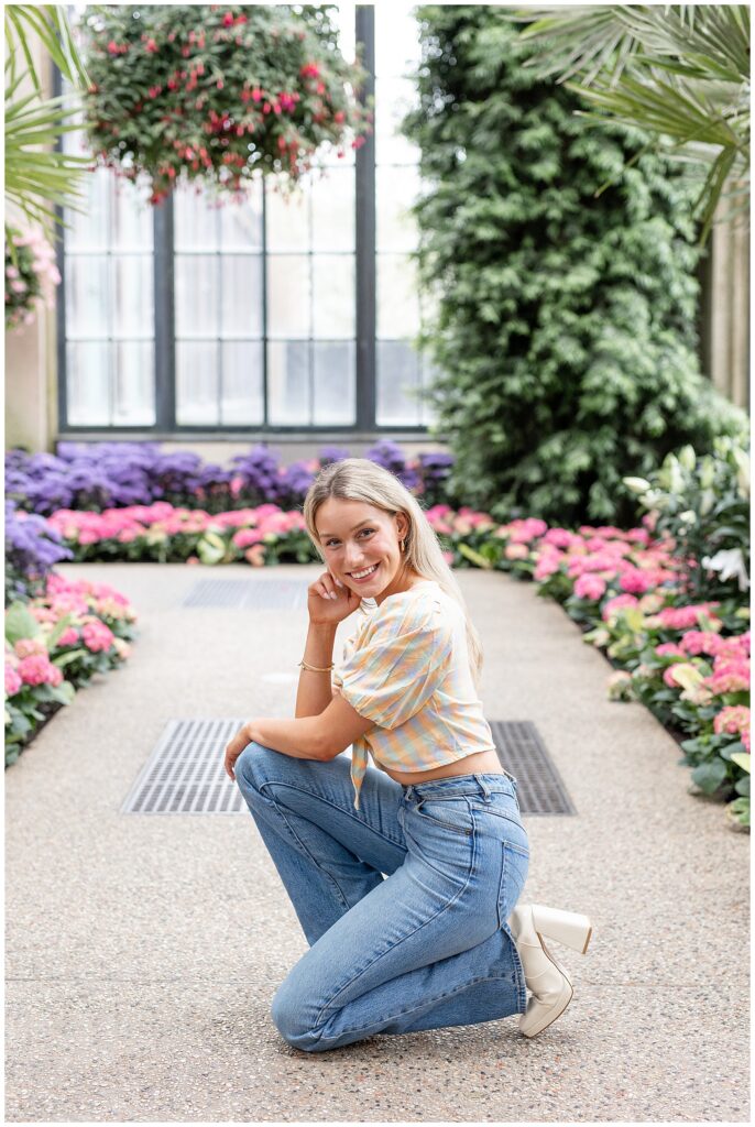 senior girl posing in aisle of arboretum and crouched down on left knee in the springtime at longwood gardens