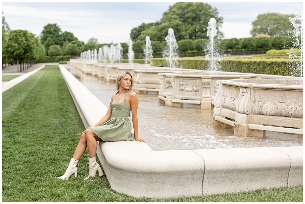senior girl sitting on concrete ledge of fountains and looking back over left shoulder at longwood gardens