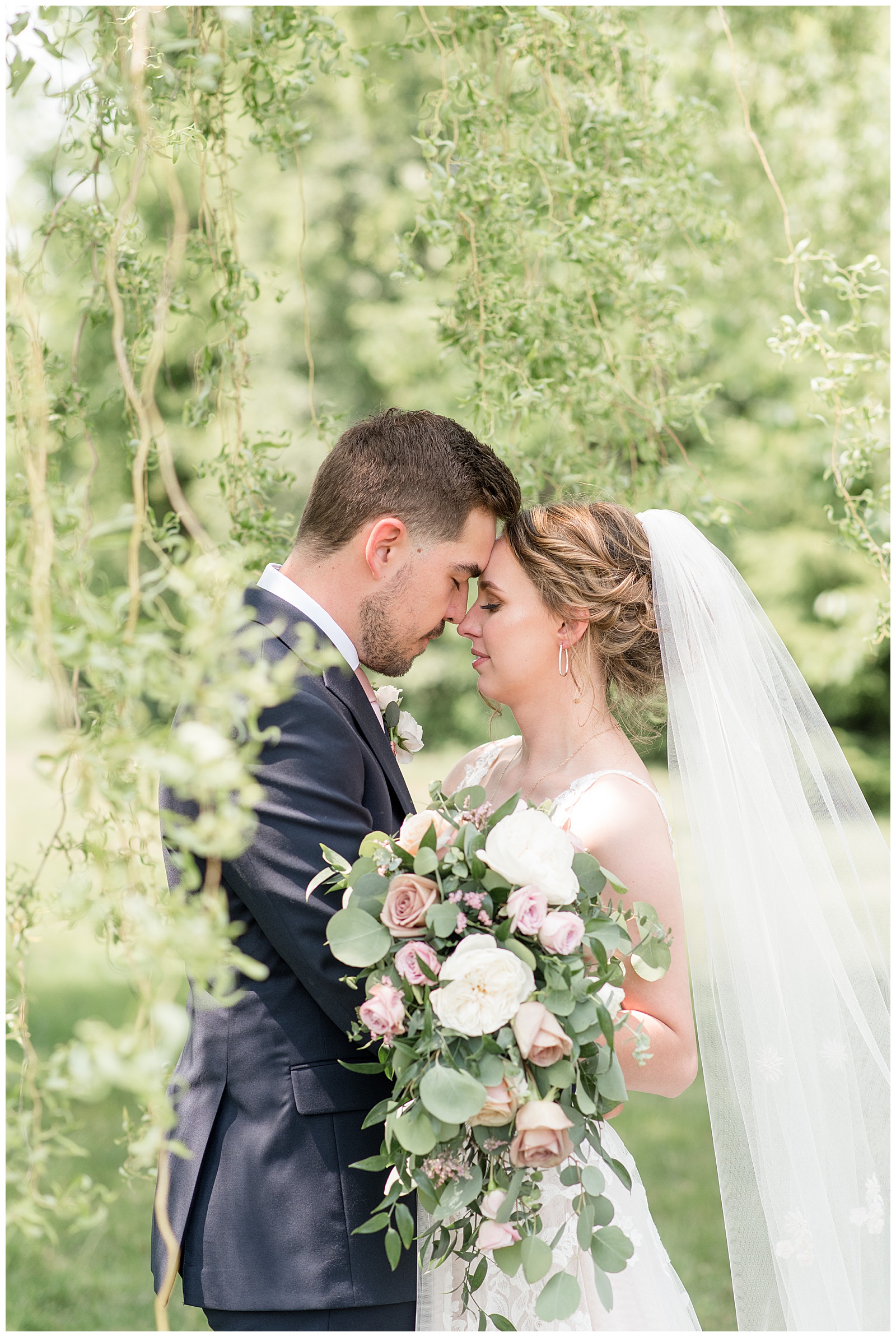 bride and groom touching foreheads together by willow tree at the barn at silverstone